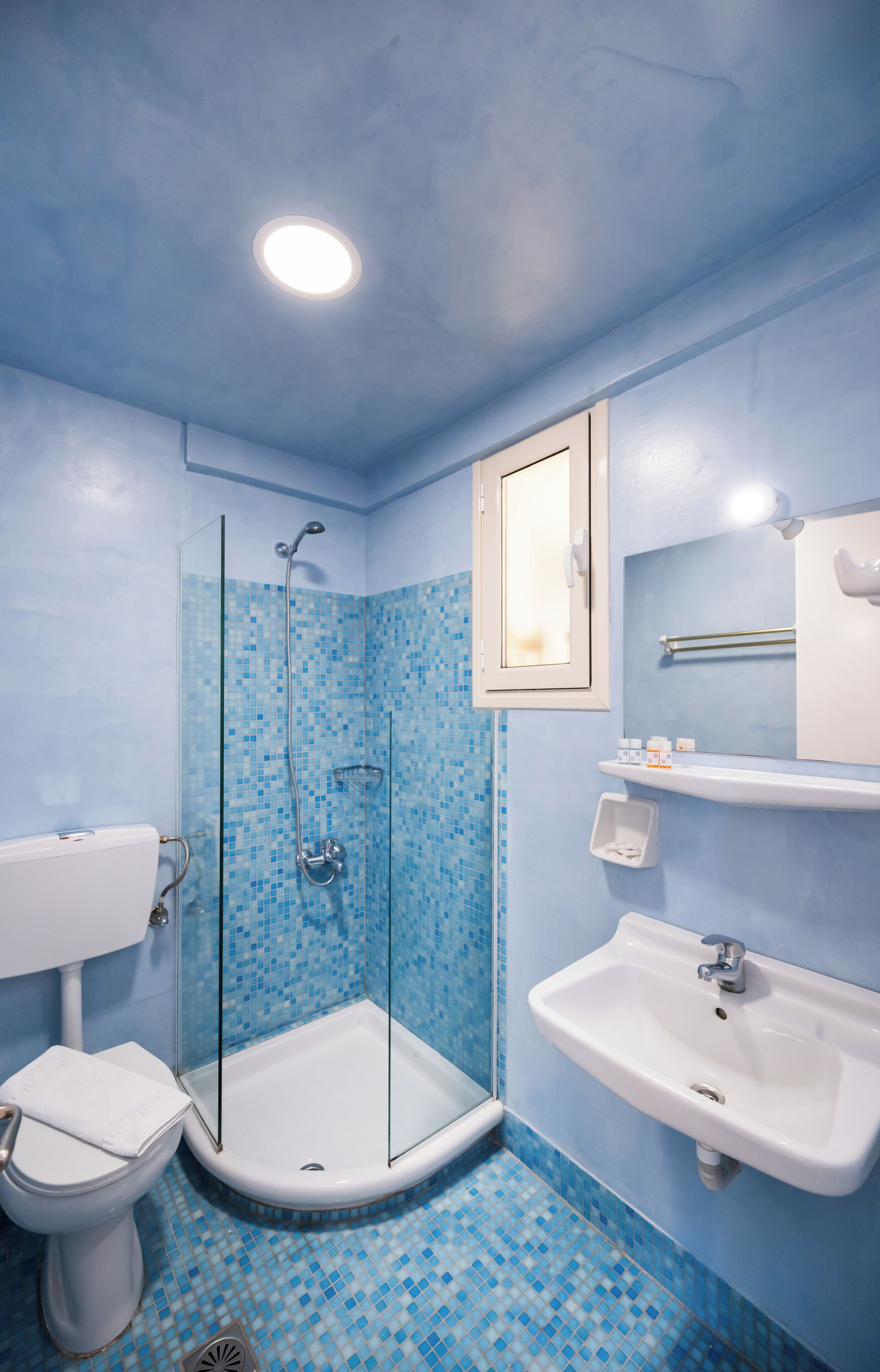 A bathroom with a glass shower enclosure, a white sink, and a toilet.