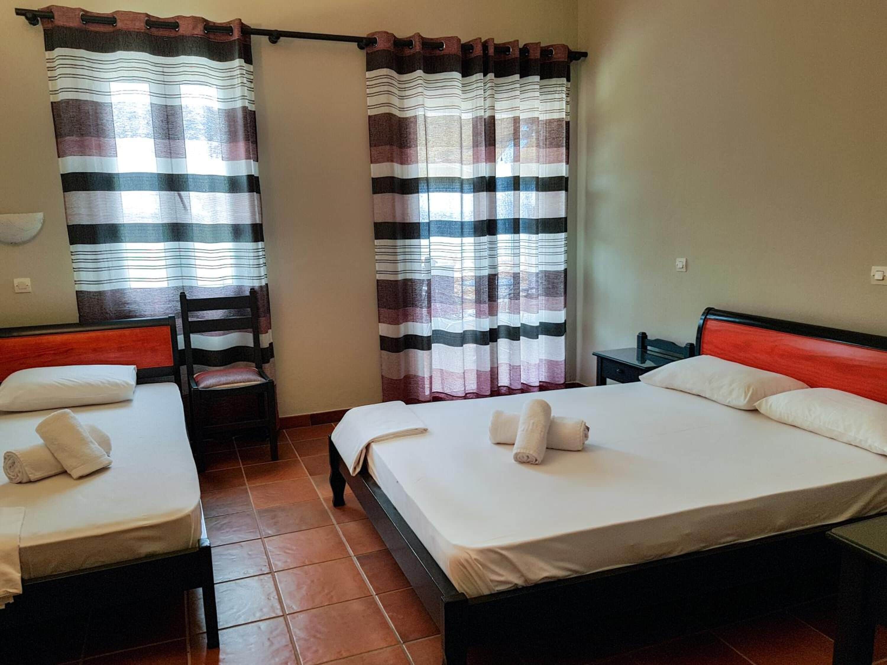 A hotel room with two beds, a chair, and curtains.