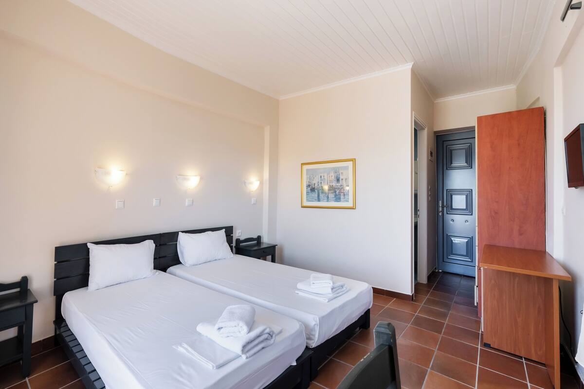 Une chambre d’hôtel avec deux lits, un bureau en bois et une porte donnant sur une autre pièce.