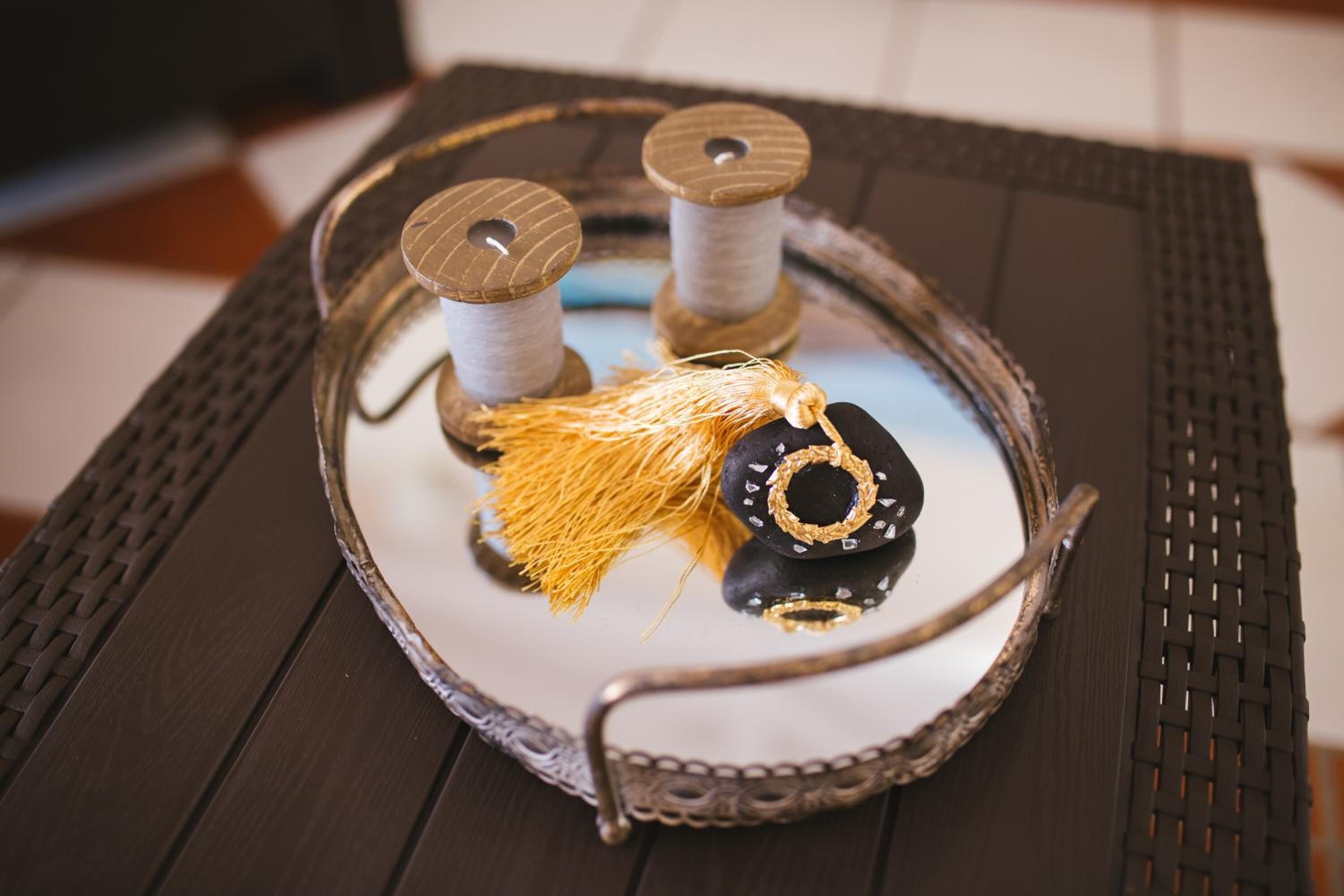 A tray with spools of thread, a decorative black and gold item, and a yellow tassel on a dark woven table.