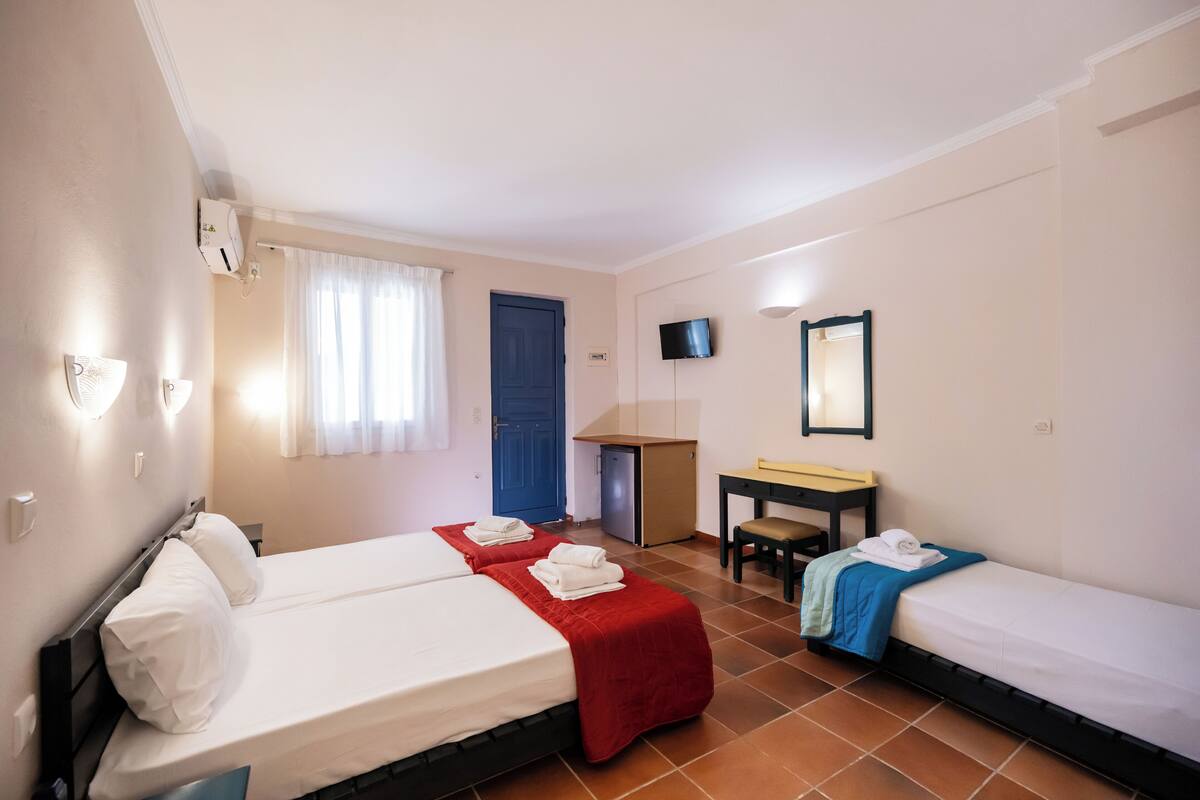 Une chambre d’hôtel avec deux lits, un bureau, une chaise, une télévision et une porte.