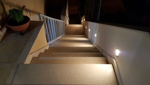 Un escalier avec une rampe, une plante en pot et des lampes fixées au mur.