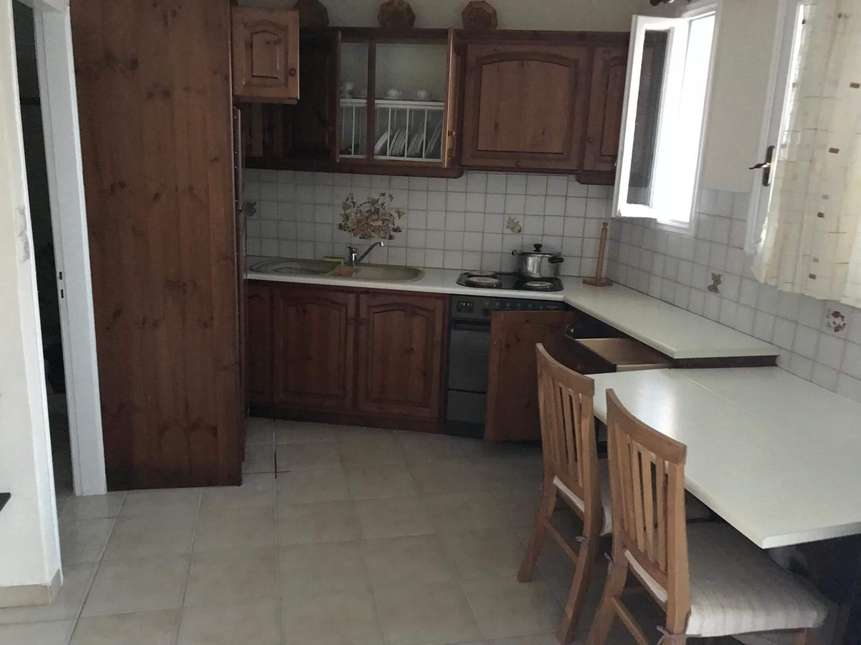 Una cucina con mobili in legno, un piano di lavoro bianco, un lavello, un fornello e una finestra con tende.