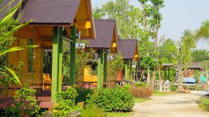 A row of wooden cabins with green pillars and corrugated metal roofs, numbered 2, 3, and 4, surrounded by lush greenery. - Nung Ni Bangkonthi (Bang Khonthi)