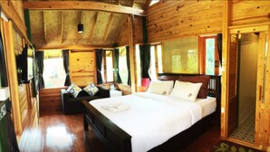 A wooden cabin bedroom with a large bed, a sofa, and a window with curtains. - Nung Ni Bangkonthi (Bang Khonthi)