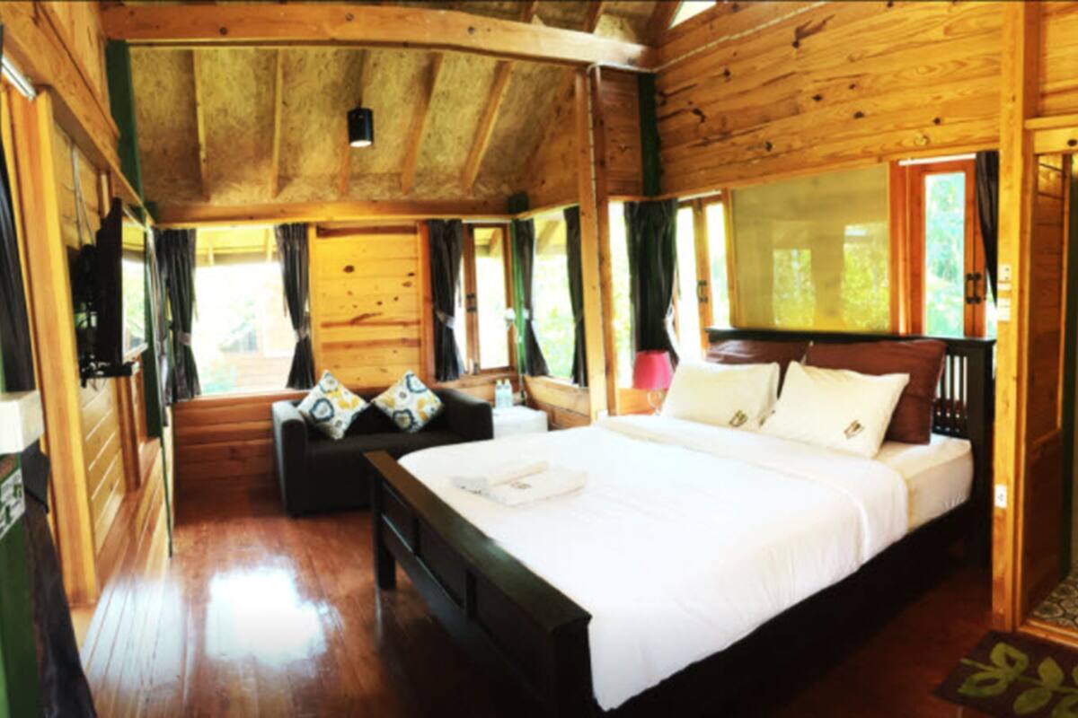 A wooden cabin bedroom with a large bed, a sofa, and a window with curtains.