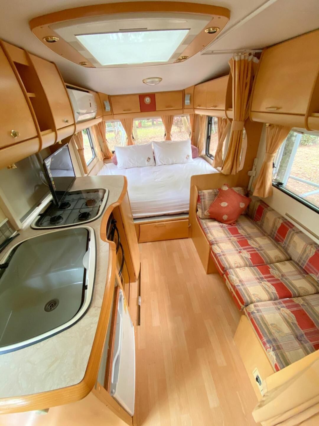 A compact RV interior with a kitchenette, a bed, and a seating area.