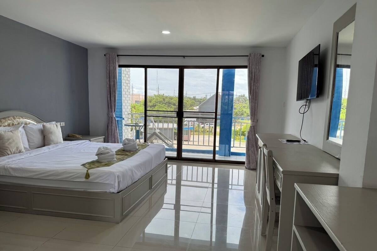 A modern hotel room with a large bed, a desk, a flat-screen TV, and a balcony with a view of the city.