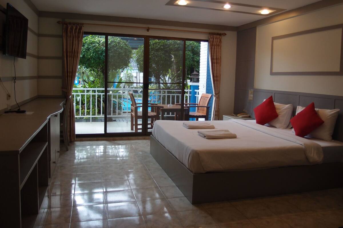 A hotel room with a bed, a desk, a chair, and a view of a pool and greenery.