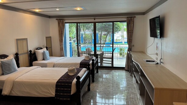 A hotel room with two beds, a TV, a desk, and a view of a pool. - Blue Garden Resort Pattaya (Pattaya)