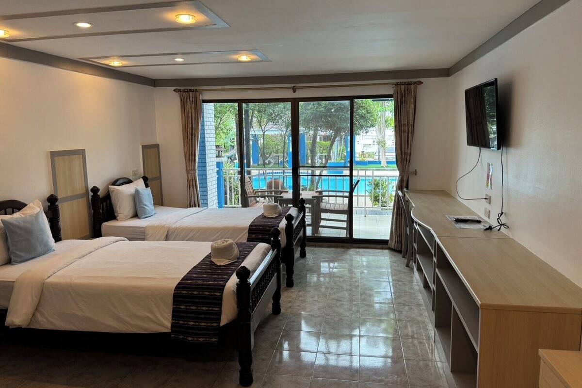 A hotel room with two beds, a TV, a desk, and a view of a pool.
