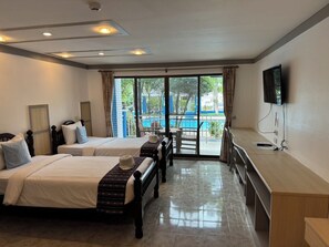 Quarto de hotel com duas camas, televisão, escrivaninha e vista para a piscina.