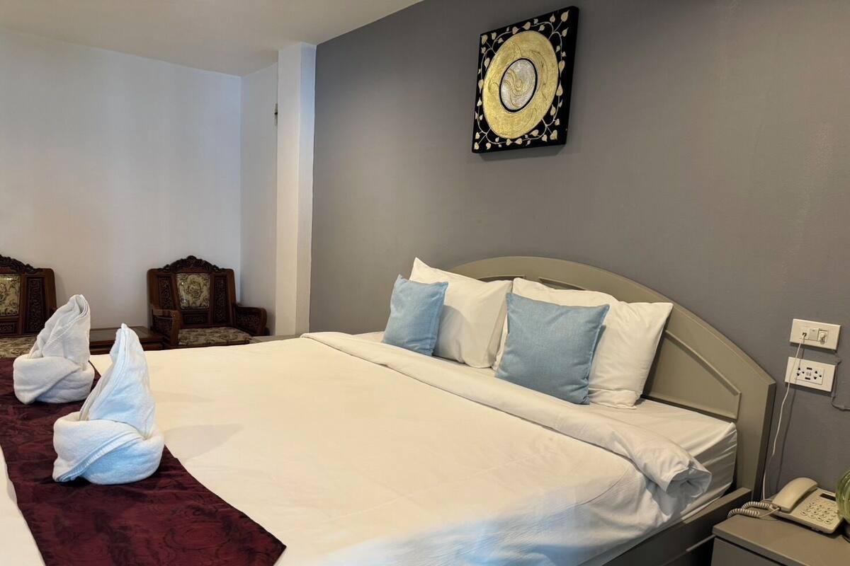A hotel room with a neatly made bed, a bedside telephone, and a wall-mounted decorative piece.