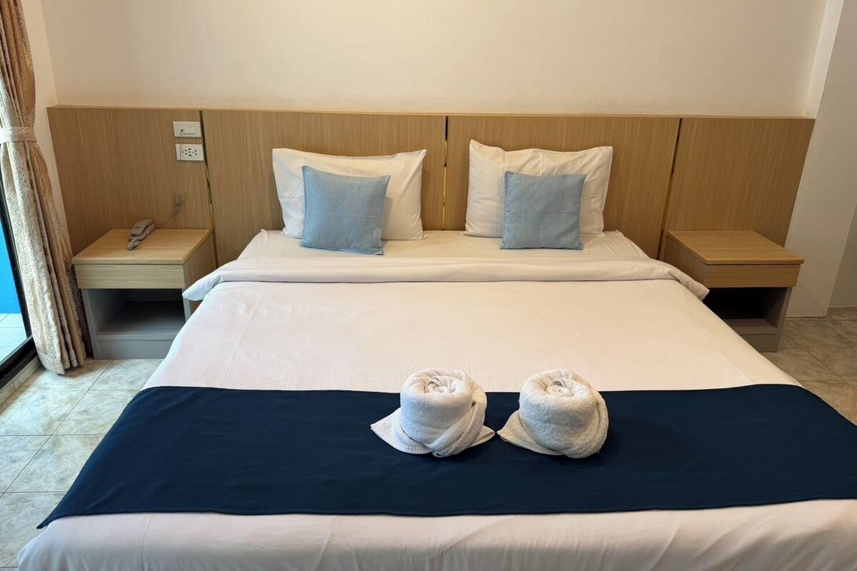 A hotel room with a large bed, two pillows, a bedside table, a telephone, and two towels on the bed.
