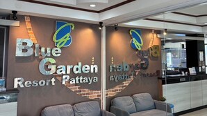 A Blue Garden Resort Pattaya reception area with a chandelier, two grey sofas, a small blue table, and a brick wall with the resort's name and logo. - Blue Garden Resort Pattaya (Pattaya)