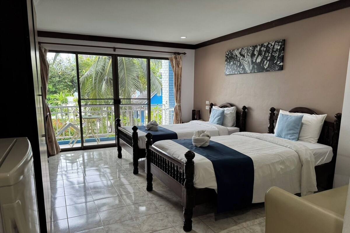 A hotel room with two beds, a balcony with a view of greenery, and a modern design.