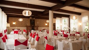 A banquet hall with multiple round tables, white tablecloths, and red chair sashes.
