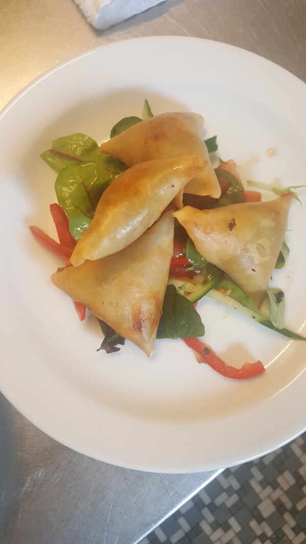 Un plato con tres pastas doradas, posiblemente samosas, acompañado de una ensalada mixta y pimiento rojo.
