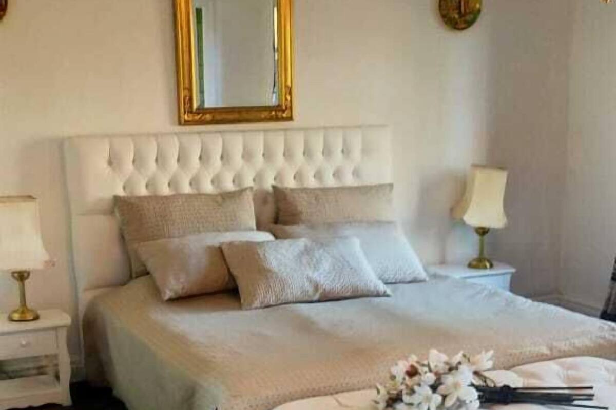 A bedroom with a large bed, a bedside table, a nightstand, a mirror, and a chandelier.