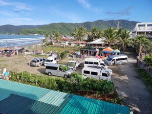 Zona costera con furgonetas estacionadas, una playa y montañas al fondo.