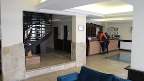 Un vestíbulo con pared de piedra, un sofá azul, una escalera y un mostrador de recepción.