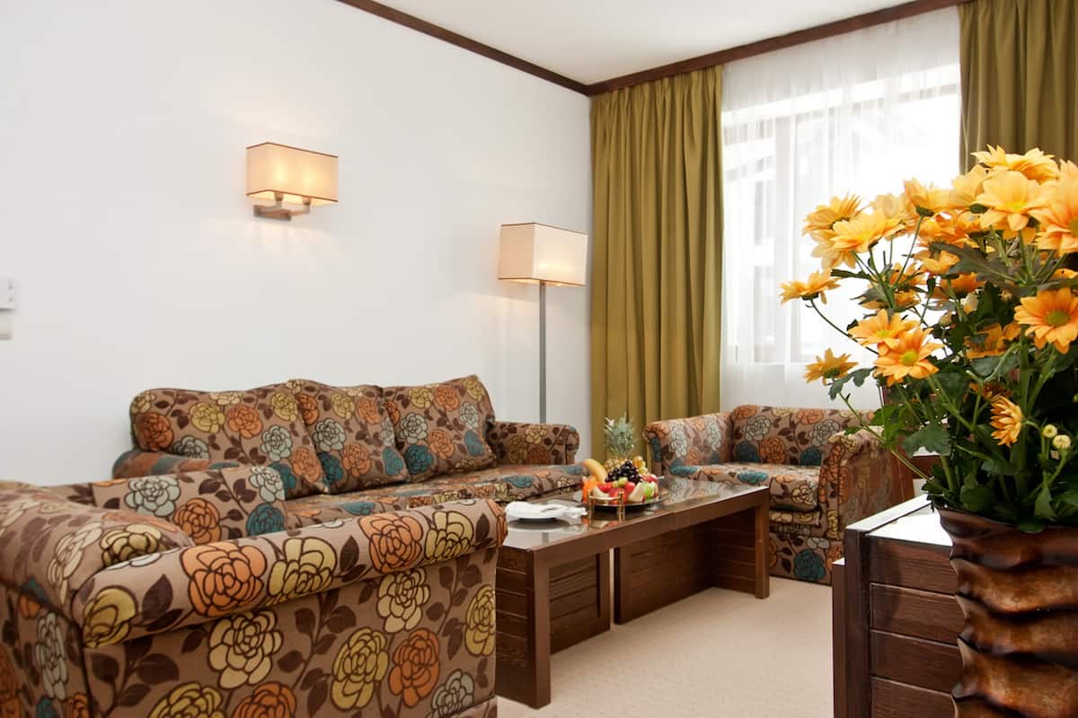 A living room with floral-patterned sofas, a coffee table with fruit, and two wall-mounted lamps.
