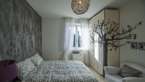 A bedroom with a bed, a chair, a wardrobe, a window with curtains, and a wall decoration. - Ritratto sul Lago (Dormelletto)
