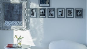 A modern room with a white armchair, a small round table with a vase of flowers, and a series of framed pictures on the wall. - Ritratto sul Lago (Dormelletto)