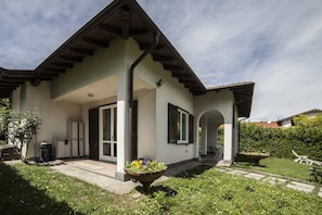 A two-story house with a covered porch, a garden with a large planter, and a clear sky. - Ritratto sul Lago (Dormelletto)