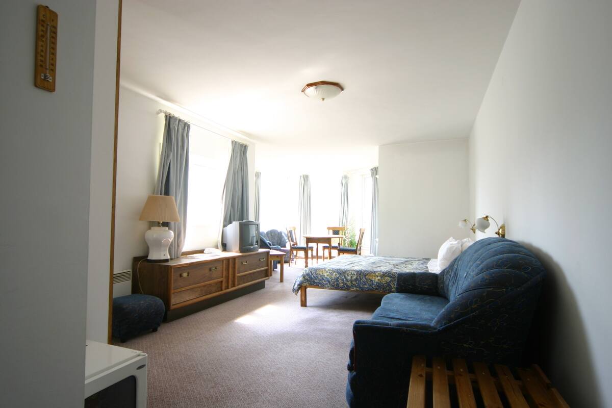 Ein Schlafzimmer mit Bett, Kommode, Fernseher und Schreibtisch mit Stuhl.