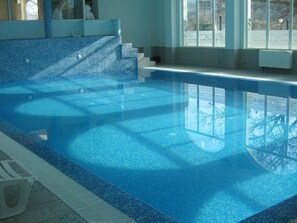 An indoor swimming pool with clear blue water, tiled steps, and windows with 'HOTEL SH' signage. - Chateau Hotel (Bansko)