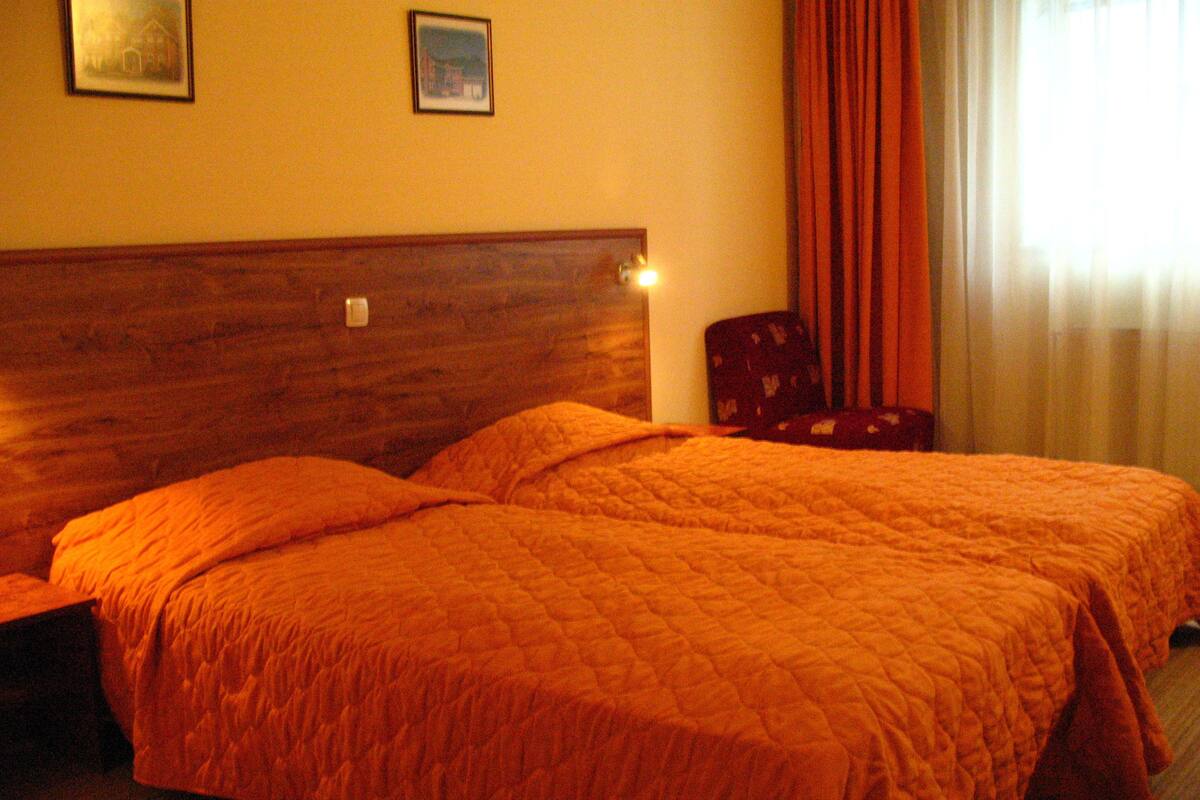 Ein Doppelbett mit Holz Kopfteil, zwei gerahmte Bilder an der Wand und ein Fenster mit Vorhängen.