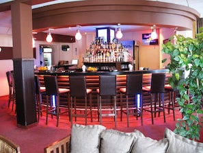 A bar area with a counter, multiple bar stools, and a variety of bottles.