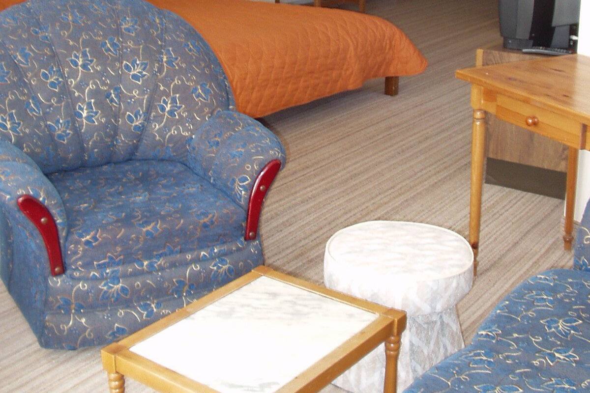 Ein Hotelzimmer mit einem Bett, einem blauen Sessel, einem Holztisch, einem Fernseher und einem kleinen weißen Hocker.
