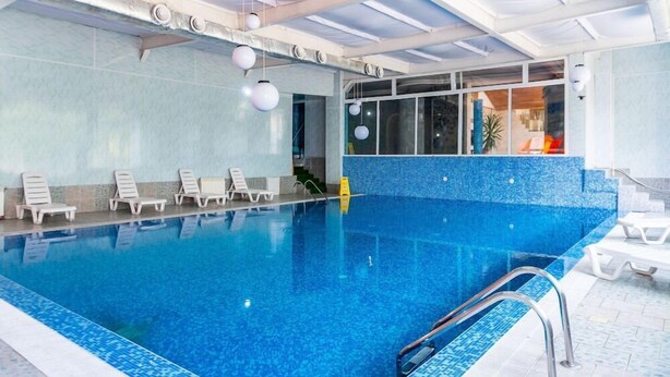 An indoor swimming pool with clear blue water, white lounge chairs, and a view of the interior through large windows. - Chateau Hotel (Bansko)