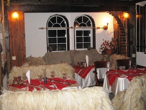 A rustic dining area with wooden walls, two arched windows, and tables set for a meal.