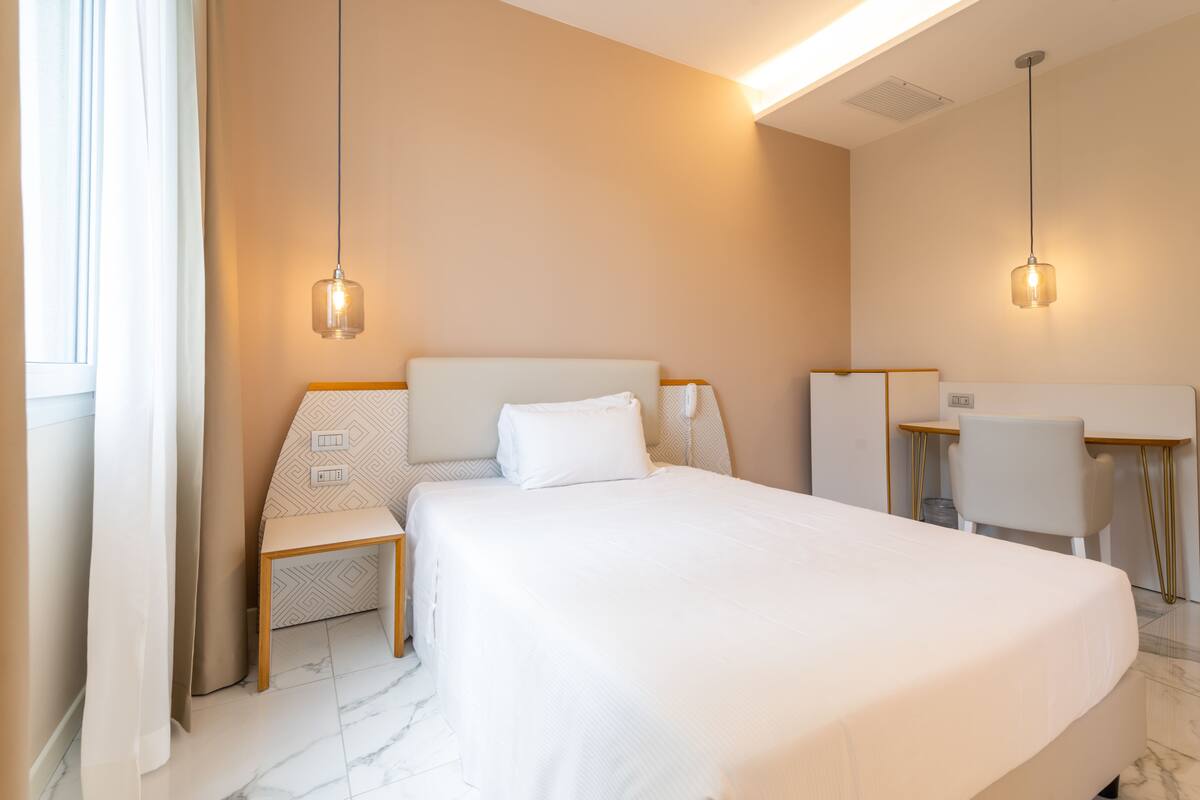 Una camera d'albergo moderna con un ampio letto, comodini, una scrivania e due lampade a sospensione.