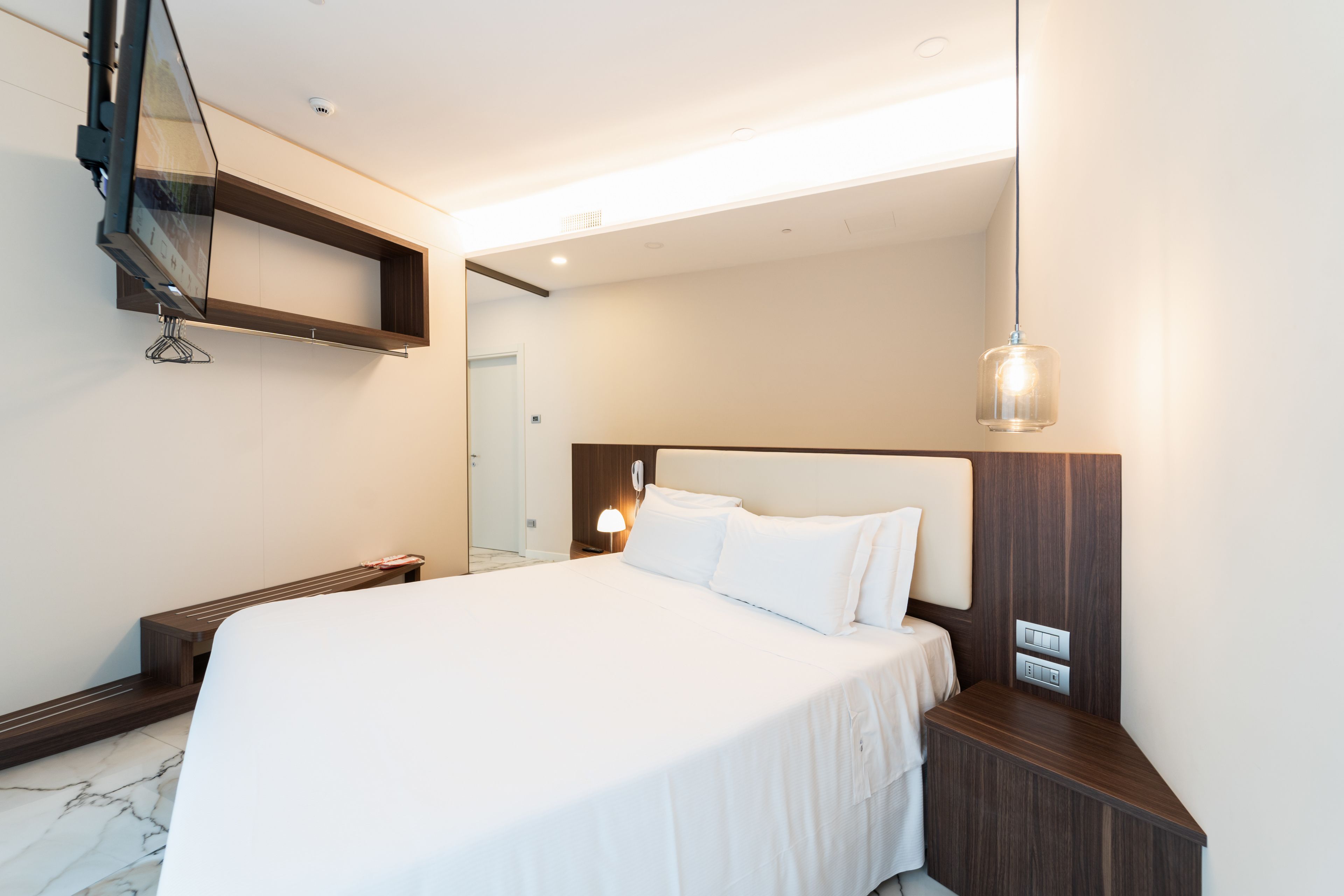 Una camera d'albergo moderna con un letto grande, un comodino e una mensola a muro sopra il letto.
