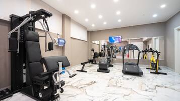 Een sportschool met diverse fitnessapparaten, waaronder een krachttrainingapparaat, loopbanden en hometrainers.