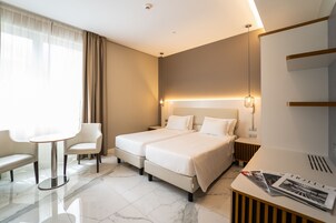 Una habitación de hotel moderna con dos camas, una mesita, una silla y un escritorio con lámpara.