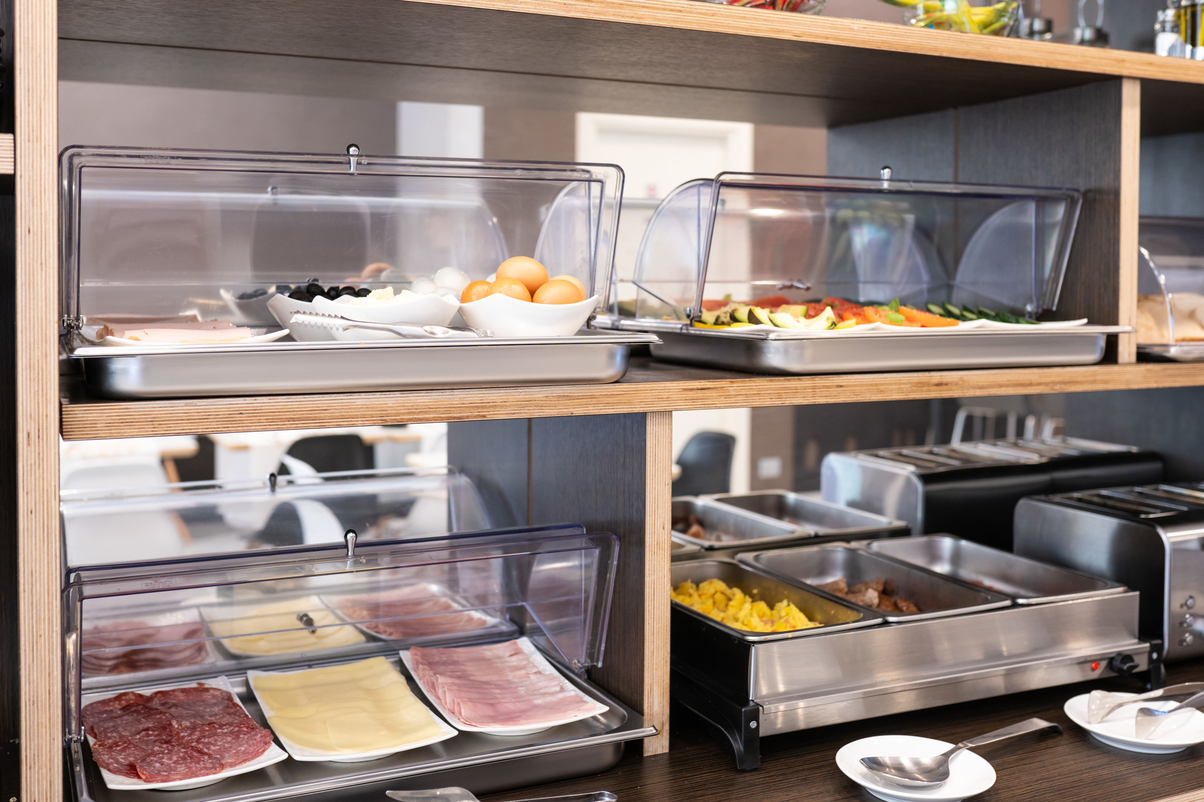 Un buffet con diversi cibi esposti in contenitori trasparenti, tra cui carni, formaggi e frutta.