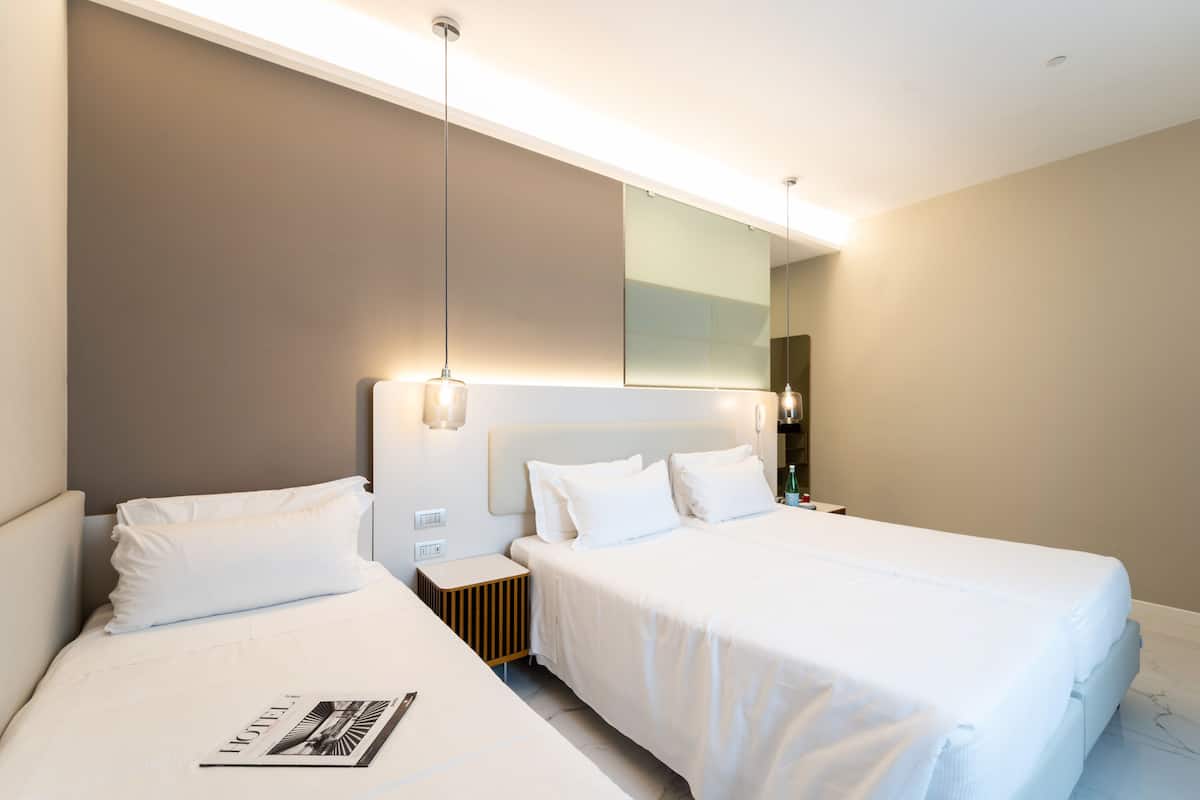 Una camera d'albergo moderna con due letti, un grande specchio e un comodino con una lampada.