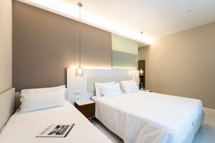 A modern hotel room with two beds, a large mirror, and a bedside table with a lamp.
