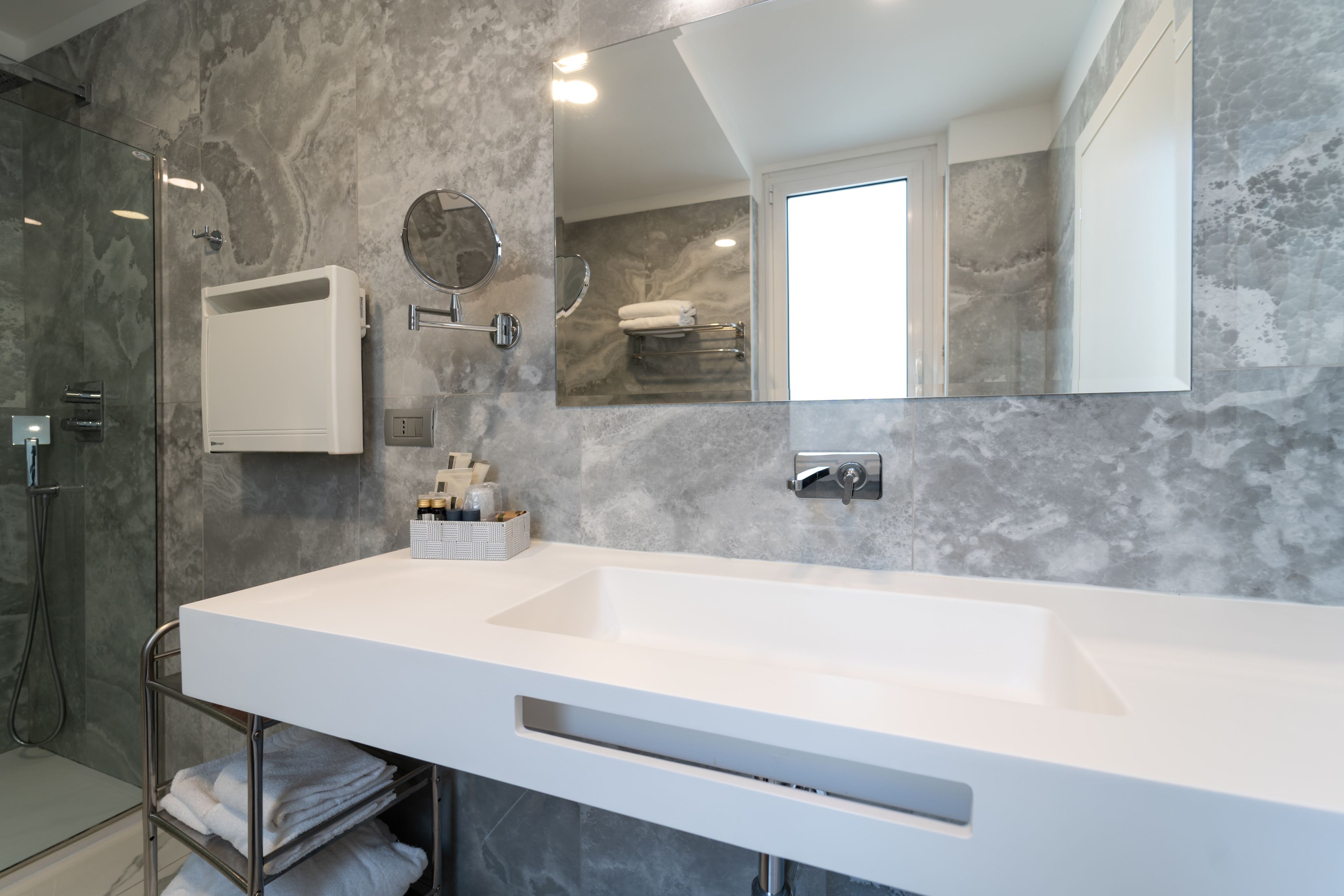 Un baño moderno con un lavamanos grande y blanco, una cabina de ducha con mampara de vidrio, un perchero y un espejo.