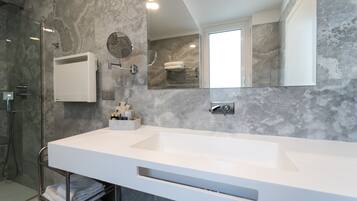 Un baño moderno con un lavamanos grande y blanco, una cabina de ducha con mampara de vidrio, un perchero y un espejo.
