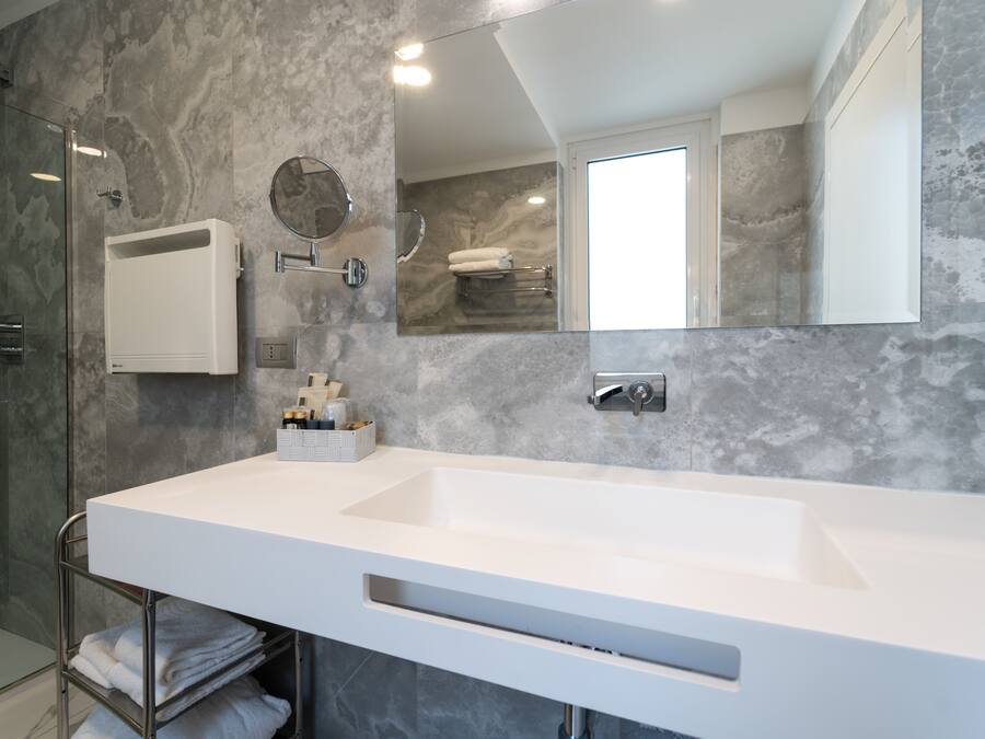 Un baño moderno con un lavamanos grande y blanco, una cabina de ducha con mampara de vidrio, un perchero y un espejo.