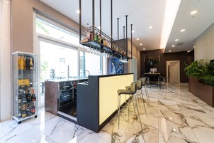Een moderne bar met een marmeren vloer, een glazen displaykast met flessen en een zithoek met barstoelen.