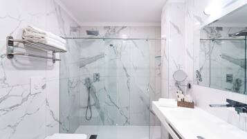 Un baño moderno con ducha de vidrio, paredes de mármol y tocador blanco con espejo.
