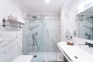 Een moderne badkamer met een douchecabine van glas, marmeren wanden en een witte wastafel met spiegel.