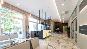 A modern hotel lobby with marble flooring, seating areas, a bar, and large windows offering a view of greenery. - Hotel Milano Castello (Milan)